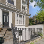 Brick townhouse with white decorative trim, black front door, stone steps, and a wrought-iron fence; potted plants on the steps.