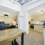 Open-plan kitchen and dining area with a wooden table, beige cabinets, and a large skylight above the space.