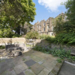 Brick townhouse row framed by a lush garden with a stone-paved patio and outdoor seating in the foreground.