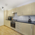 Kitchen with light wood cabinets, black countertop, and white tiled backsplash surrounding a gas stove and oven.