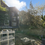 Brick townhouse with dense greenery and a white metal plant stand in the sunny garden foreground.