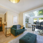 Bright living room with a skylight and large windows, green sofa, and a home office area with a desk and chair in the corner.