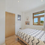Bright bedroom with a white-and-navy wavy duvet, wooden floor, and a large window with light curtains.